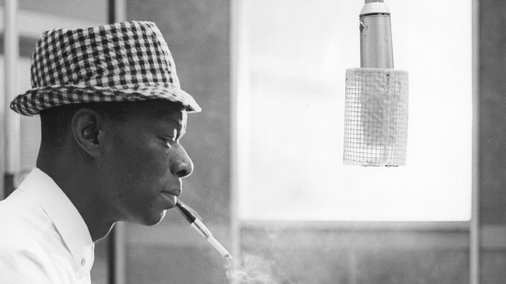Nat King Cole with a cigarette in his mouth in front of a microphone in a recording booth