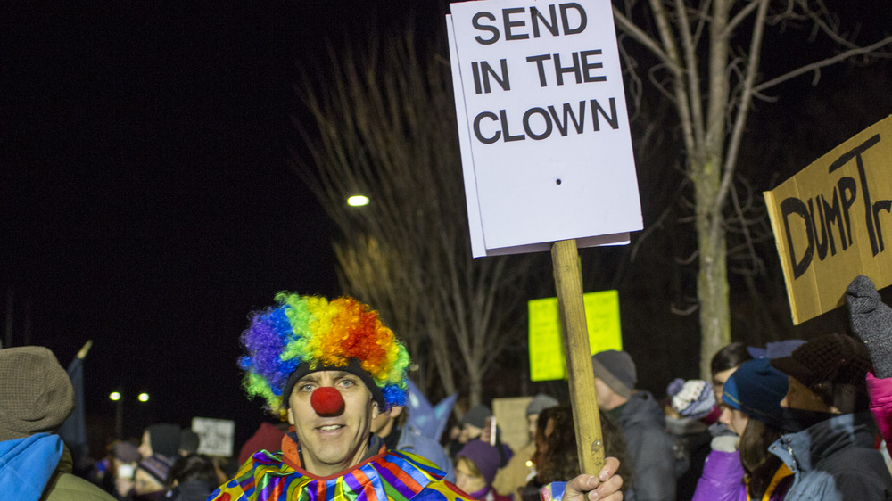 A protester dressed as a clown holding a send in the clowns sign