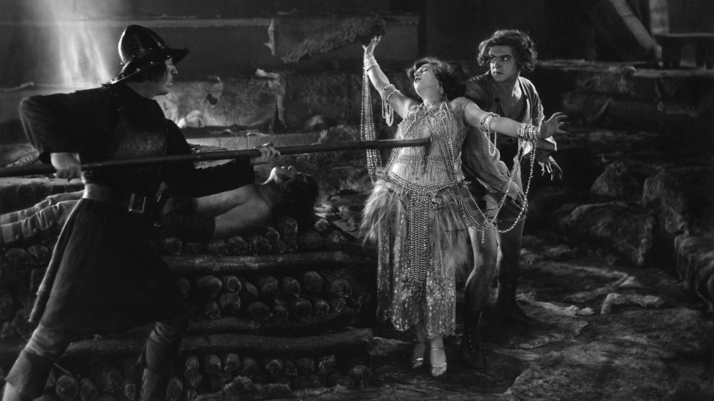 An exotically-dressed woman meets her end at the end of a long lance, as a soldier stabs her through the heart. The scene is from an unknown silent film.