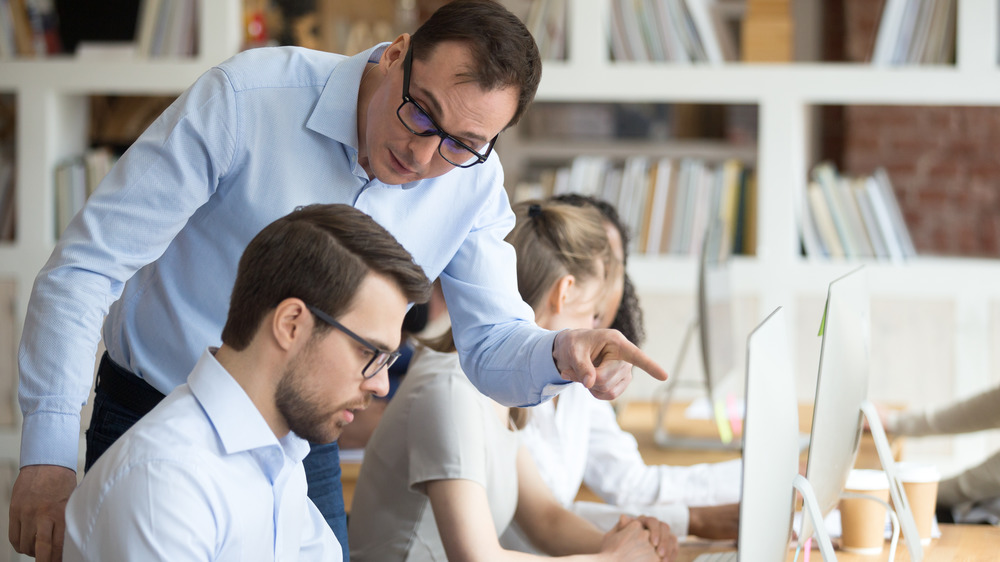 Angry boss hovering over and scolding an employee at work on their computer