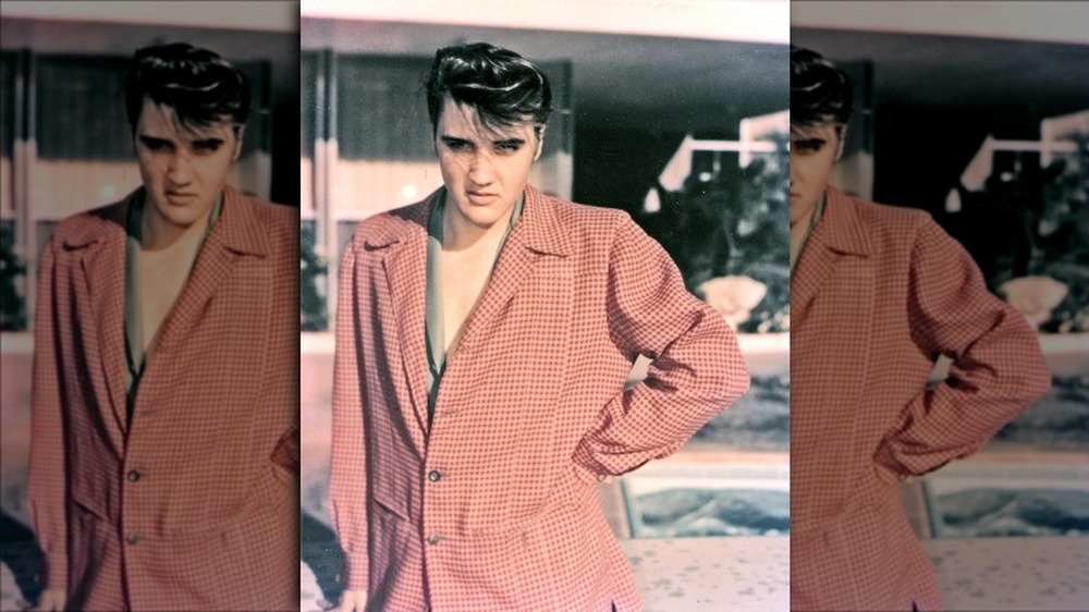 Elvis posing for a photograph in a pink/red gingham blazer