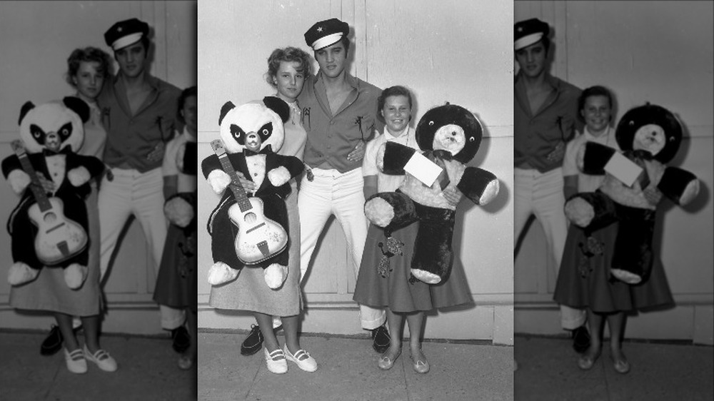 Elvis Presley posing for a photo in between two young girl fans holding teddy bears