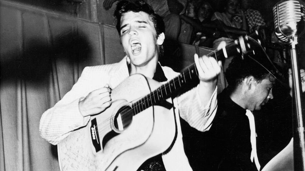 Elvis playing the guitar and singing actively on stage