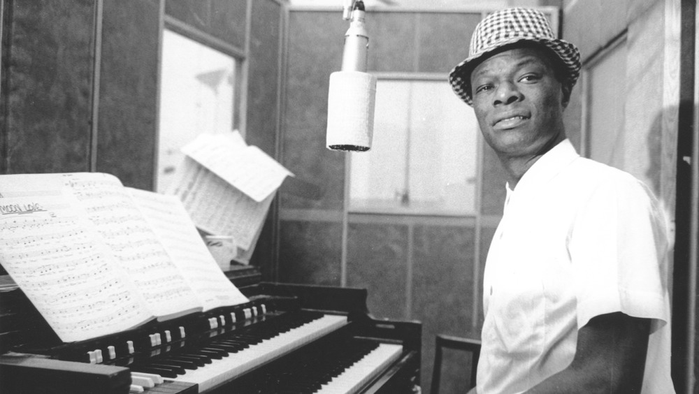 Nat King Cole sitting at a piano and in front of a microphone in a recording booth