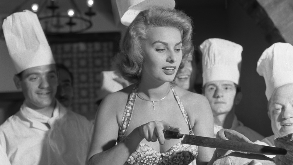 Sophia Loren cutting in a kitchen, surrounded by chefs