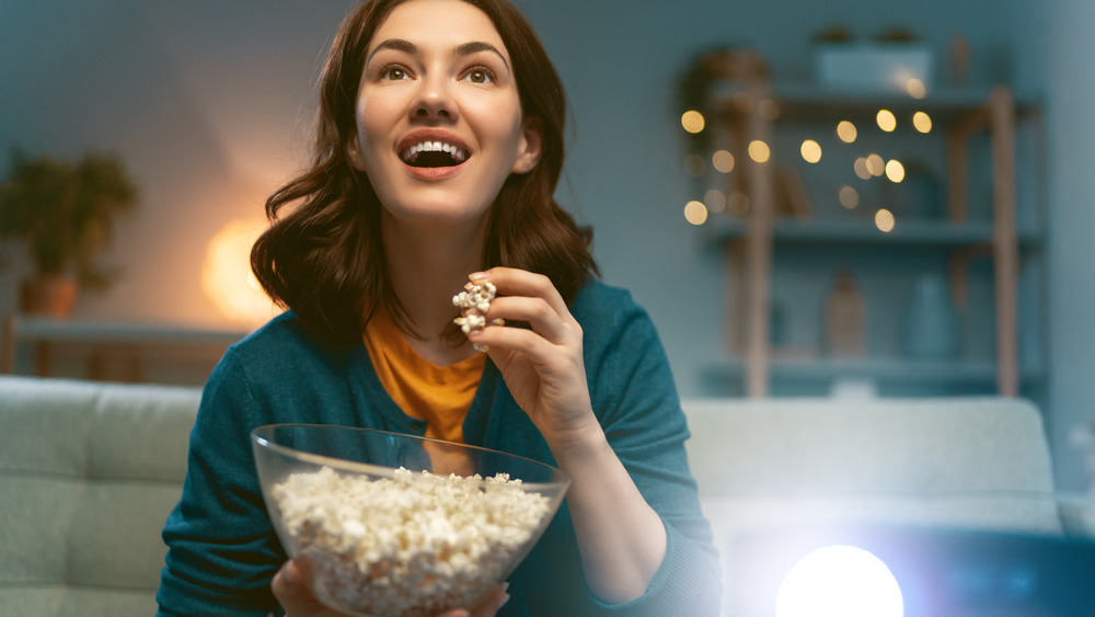 Woman eating popcorn, watching projector 