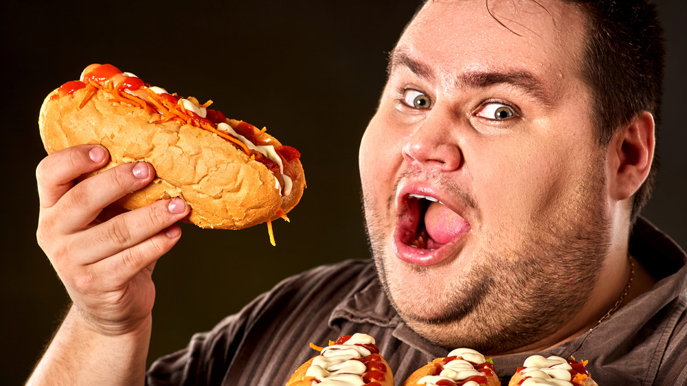 Overweight man holding multiple hot dogs
