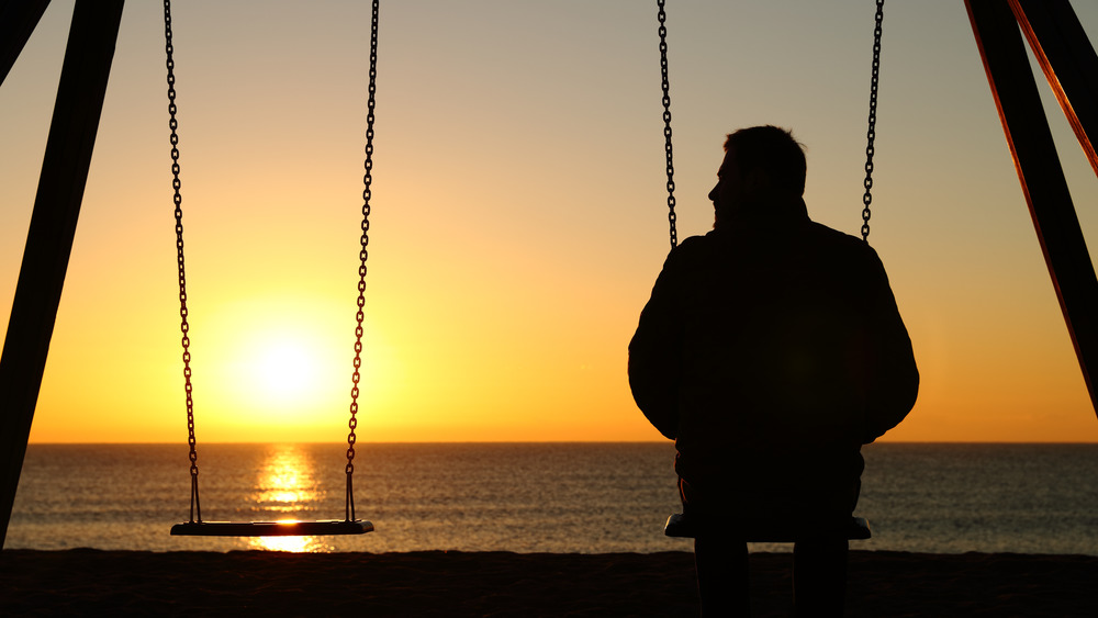 man on swingset beside empty swing