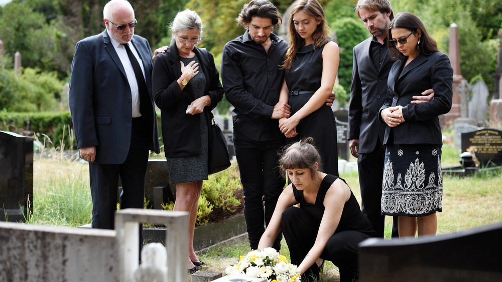 A family around a grave, one placing flowers