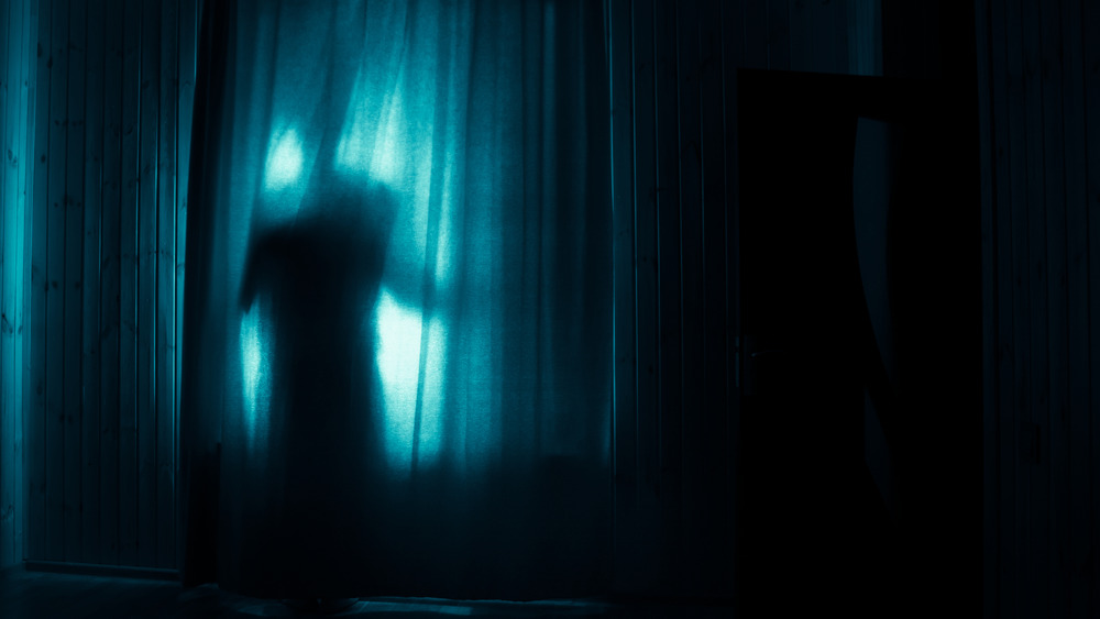 A figure hiding behind curtains
