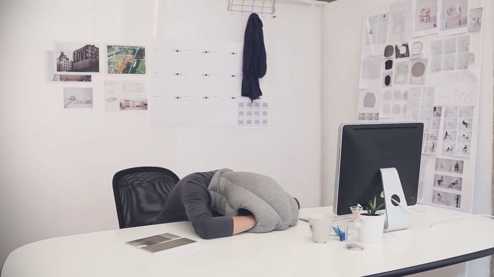 Someone napping using ostrichpillow at their office desk