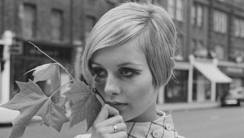 Twiggy in the streets holding a branch to her face