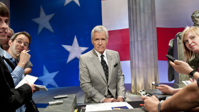 Alex Trebek at a table with Jeopardy! contestants 