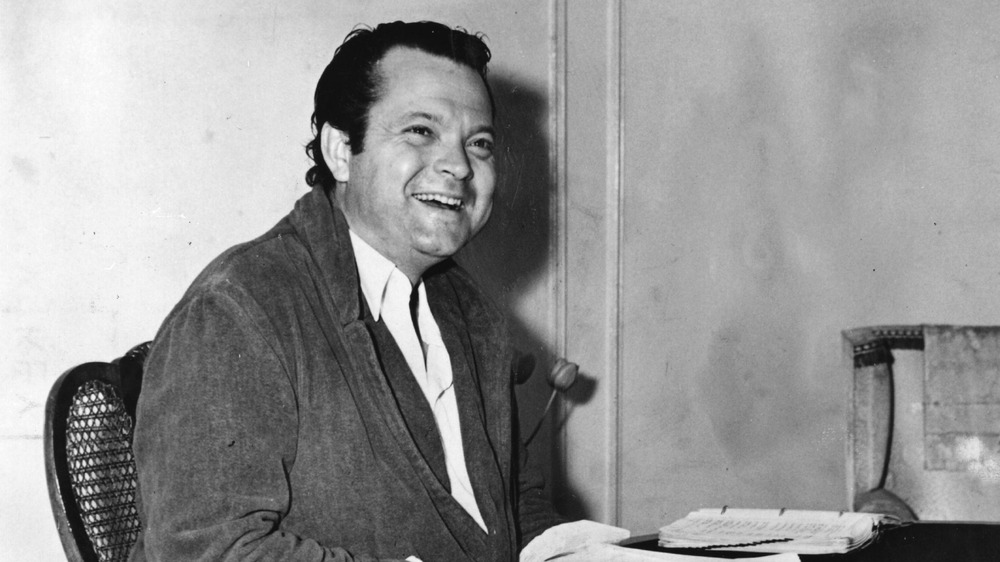 A smiling Orson Welles studies a script