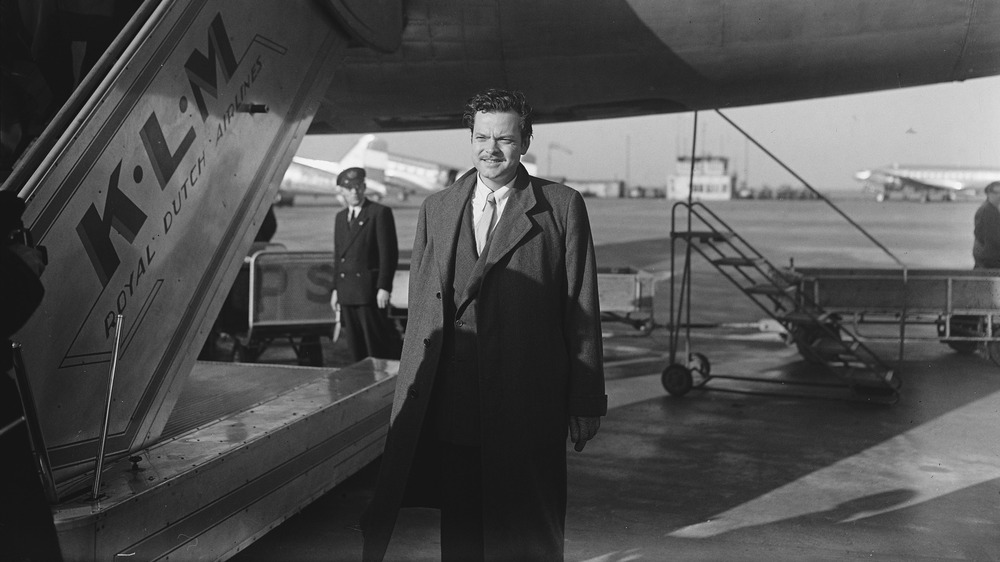 Orson Welles standing next to a plane, 1948