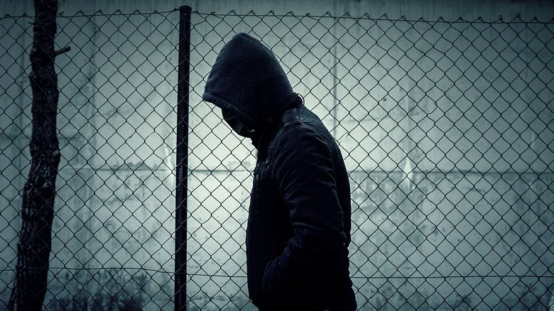 Hooded figure walking by fence