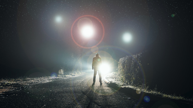 UFO concept. Glowing orbs, floating above a misty road at night. With a silhouetted figure looking at the lights.