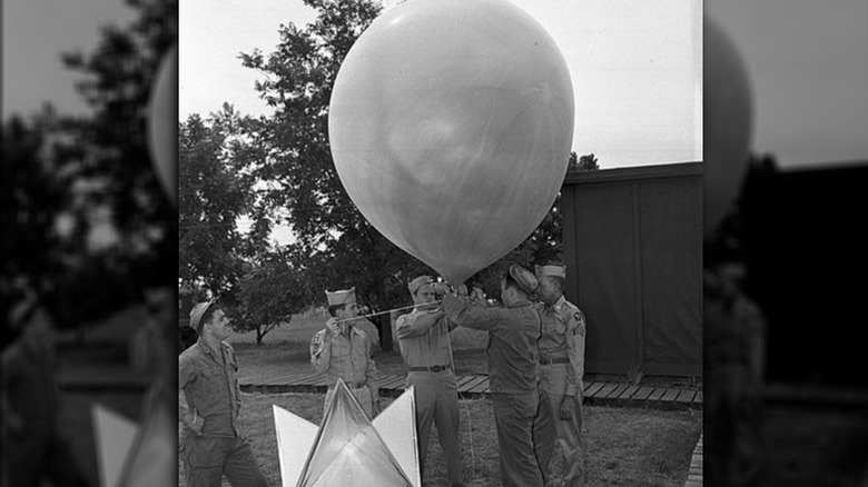 Five airmen attach a radar device to a weather balloon
