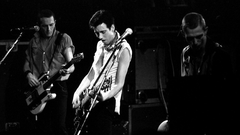 Cropped photo by Helge Øverås of Joe Strummer, Mick Jones, and Paul Simonon of The Clash onstage in 1980, CC BY-SA 4.0