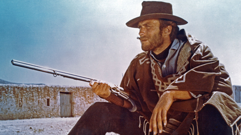 Clint Eastwood sitting smoking a cigar and pointing a gun into the distance 