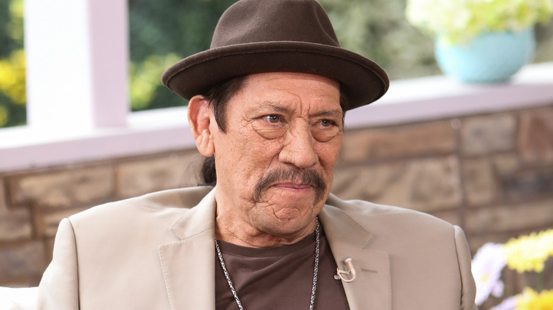 Danny Trejo in brown suit and hat, seated