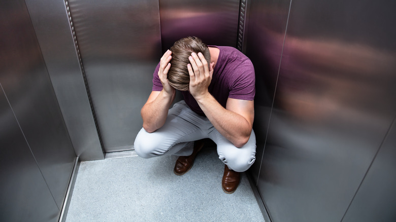 Man crouched in anxiety in elevator