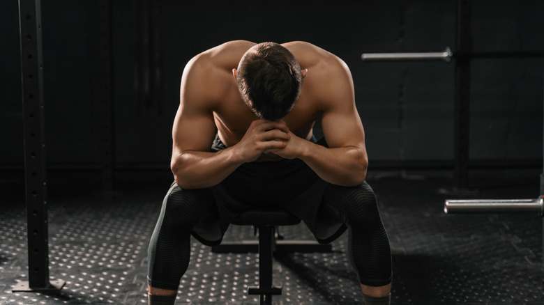 Weightlifter sitting on weight bench head in hands