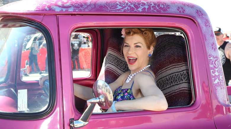 Woman dressed in vintage style smiling through window of pink car