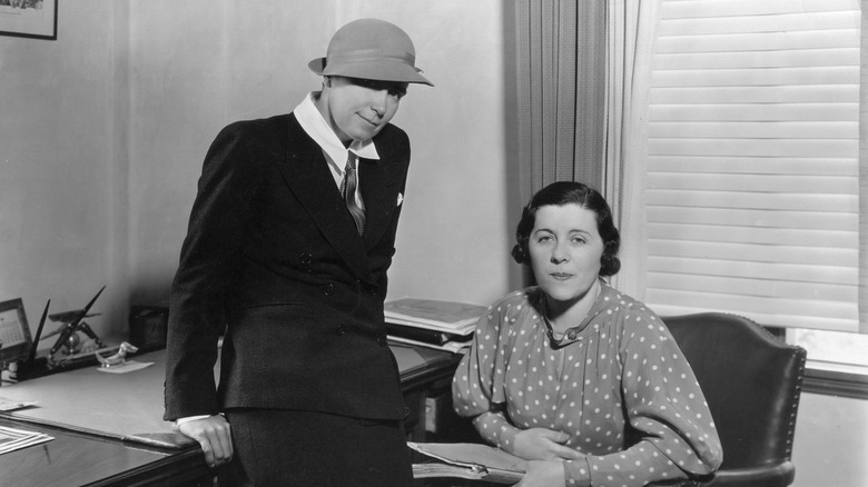 Dorothy Arzner leaning on a desk next to seated friend