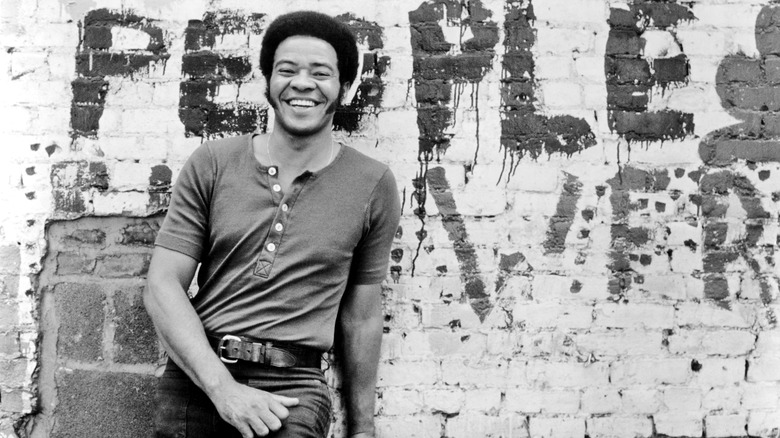 Bill Withers smiling in front of graffitied wall