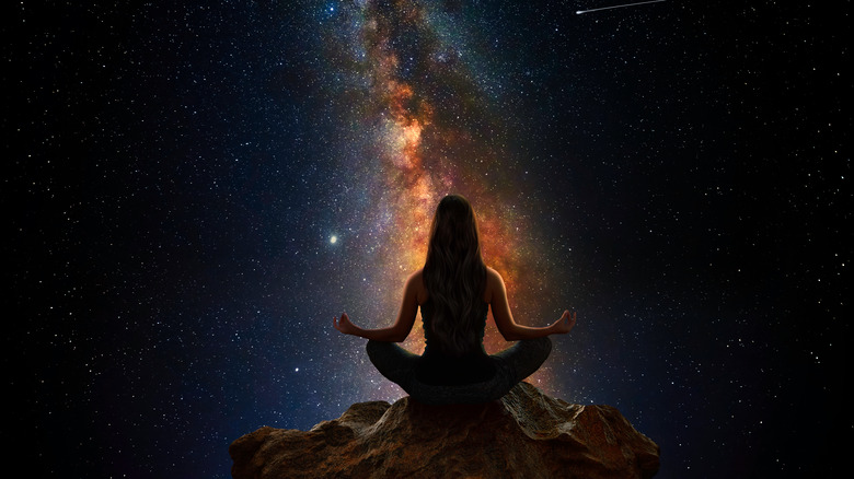 Woman sitting in meditative pose against stars