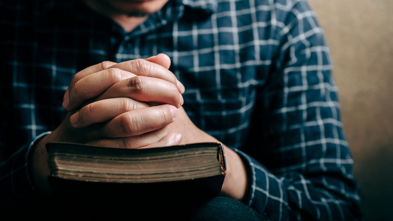 hands folded in prayer atop a bible