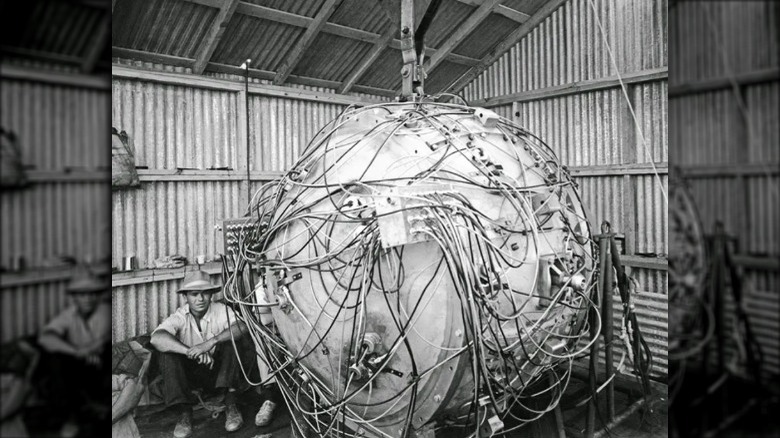 Gadget, the first atomic bomb, with man sitting next to it