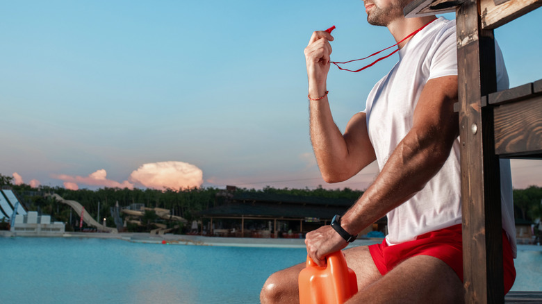 Lifeguard sitting by water with whistle raised