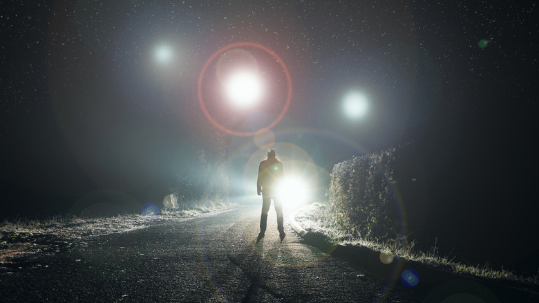 man standing in road, looking at lights in the sky