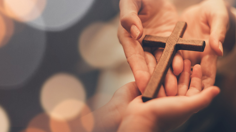 Hands passing a wooden cross