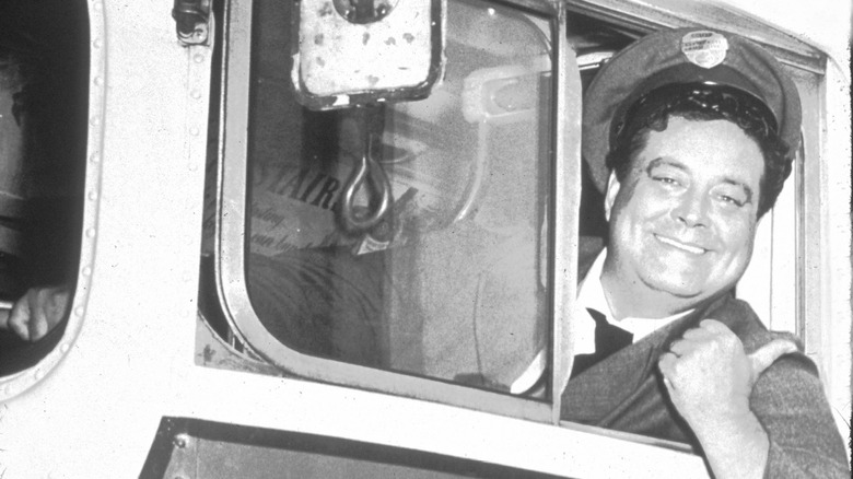 Jackie Gleason as Ralph Kramden posing in a bus
