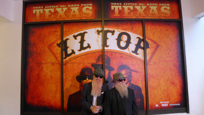 Billy Gibbons and Dusty Hill standing in front of ZZ Top poster