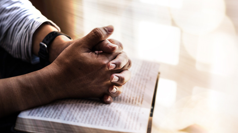 Folded hands praying over the bible