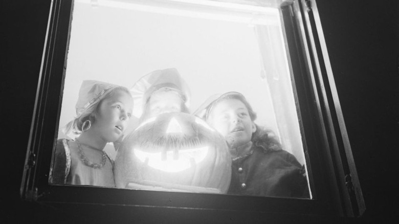 Three girls surrounding Halloween pumpkin in a window