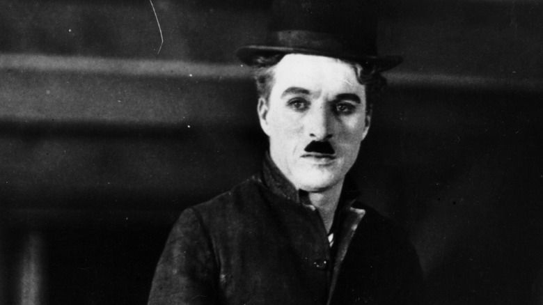 Charlie Chaplin standing before dark background