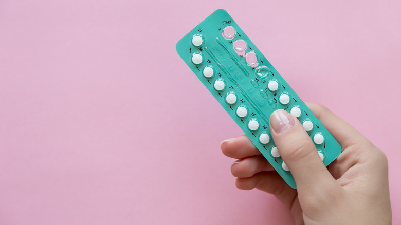 Hand holding birth control pills against pink wall