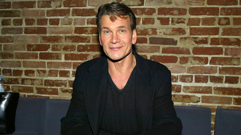 Patrick Swayze smiling in front of brick wall