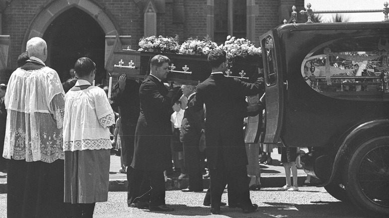 Funeral service with pallbearers putting coffin in hearse