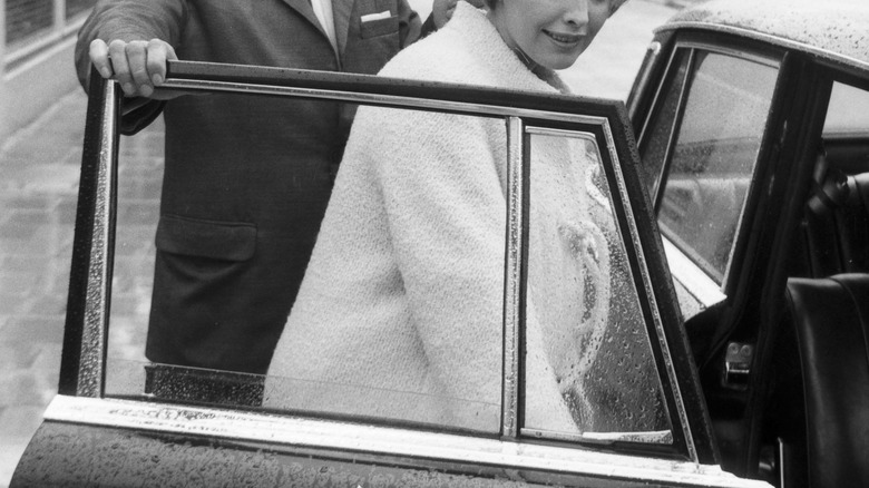 Man holding a car door open for a woman 1960s