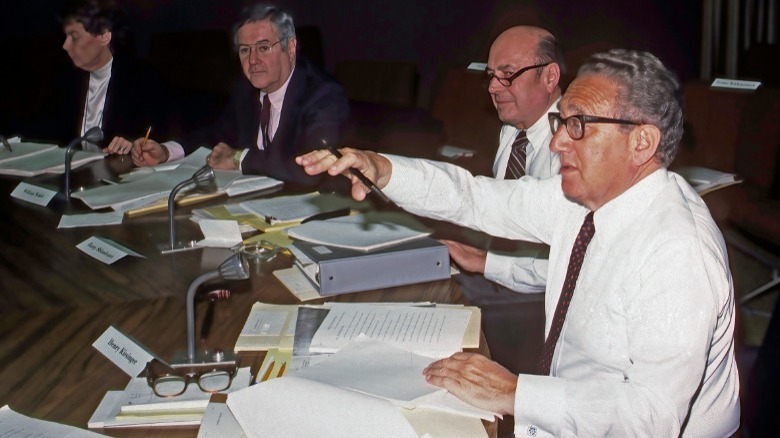 Kissinger at meeting with hand raised