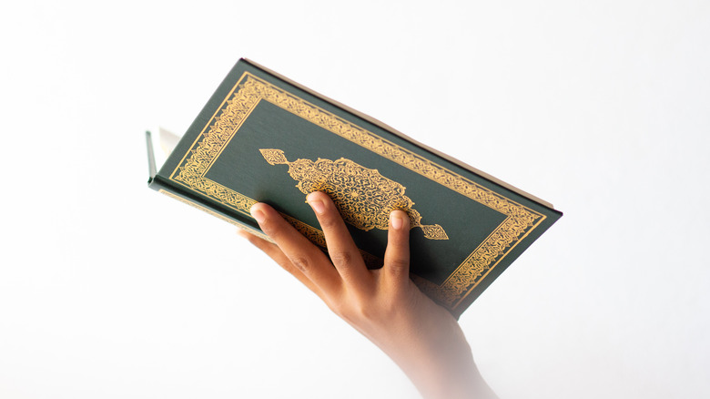 Hand holding Quran against white background